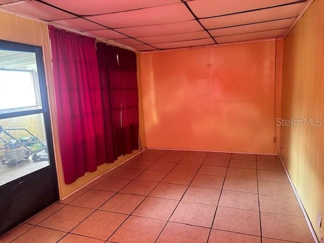 unfurnished room featuring a paneled ceiling, wood walls, and tile patterned flooring