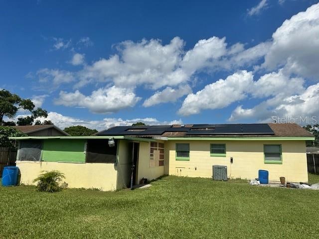 back of house with solar panels and a lawn