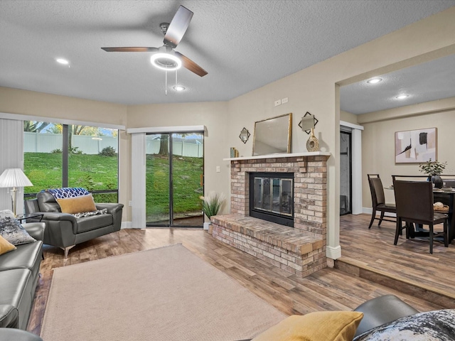 living room with a textured ceiling, ceiling fan, a fireplace, and hardwood / wood-style flooring