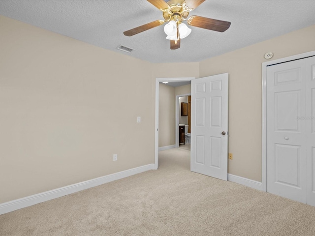 unfurnished bedroom with ceiling fan, light colored carpet, a textured ceiling, and a closet