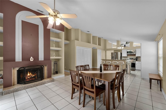 dining area with built in shelves, ceiling fan with notable chandelier, light tile patterned floors, a large fireplace, and high vaulted ceiling