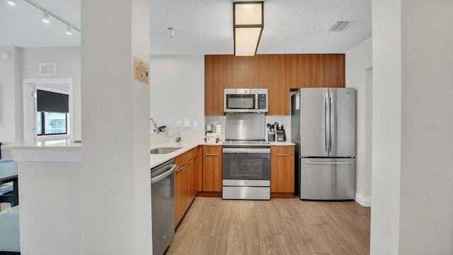 kitchen featuring sink, a textured ceiling, track lighting, stainless steel appliances, and light hardwood / wood-style floors