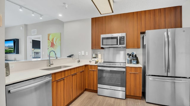 kitchen with sink, kitchen peninsula, a textured ceiling, light hardwood / wood-style flooring, and appliances with stainless steel finishes