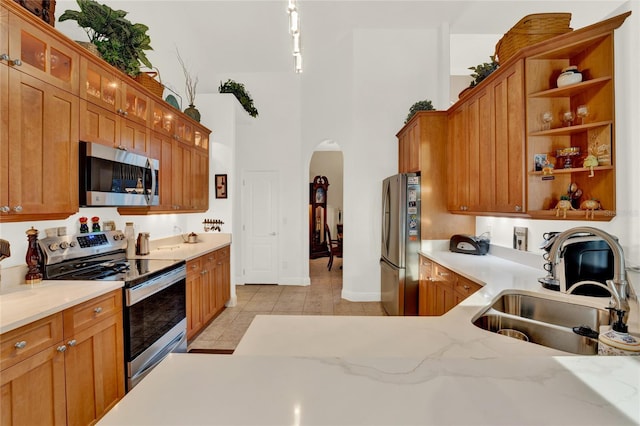 kitchen featuring sink, stainless steel appliances, light stone counters, a towering ceiling, and light tile patterned floors