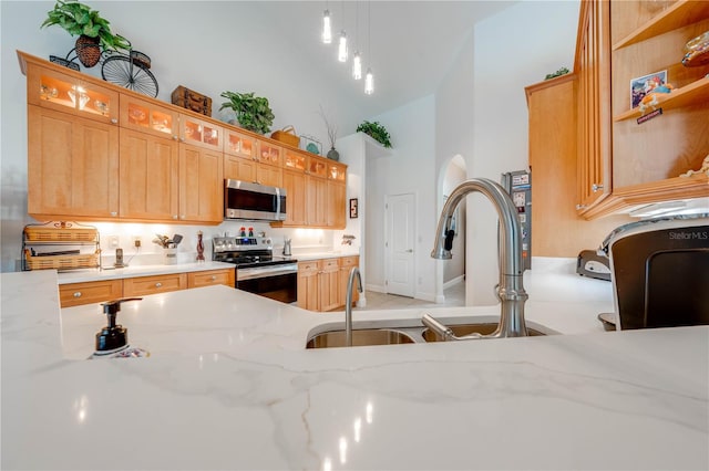 kitchen featuring light stone countertops, sink, stainless steel appliances, high vaulted ceiling, and decorative light fixtures