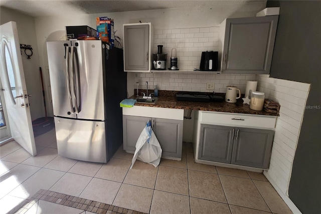 kitchen with tasteful backsplash, sink, gray cabinets, stainless steel refrigerator, and light tile patterned flooring