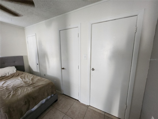 tiled bedroom with ceiling fan, crown molding, a textured ceiling, and multiple closets