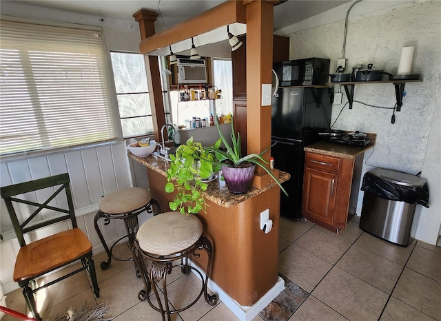 kitchen featuring tile patterned floors, a breakfast bar, and black appliances