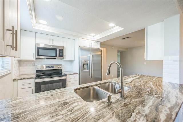 kitchen with white cabinets, appliances with stainless steel finishes, sink, and a tray ceiling