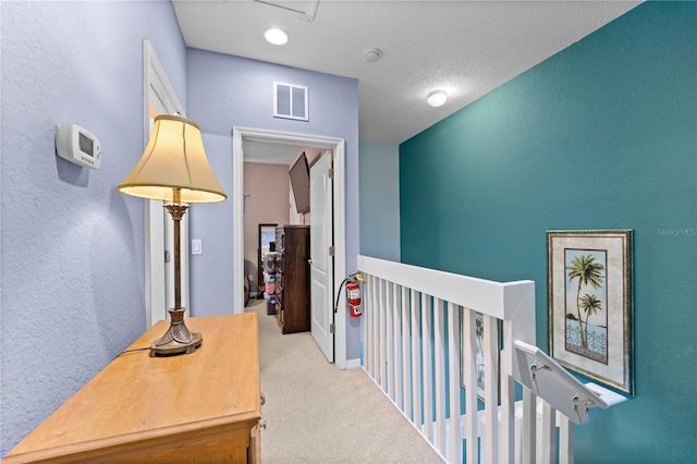 corridor with a textured ceiling and light colored carpet