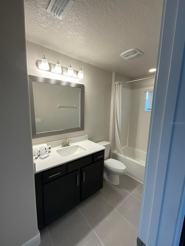 full bathroom featuring shower / bath combo with shower curtain, vanity, a textured ceiling, tile patterned flooring, and toilet