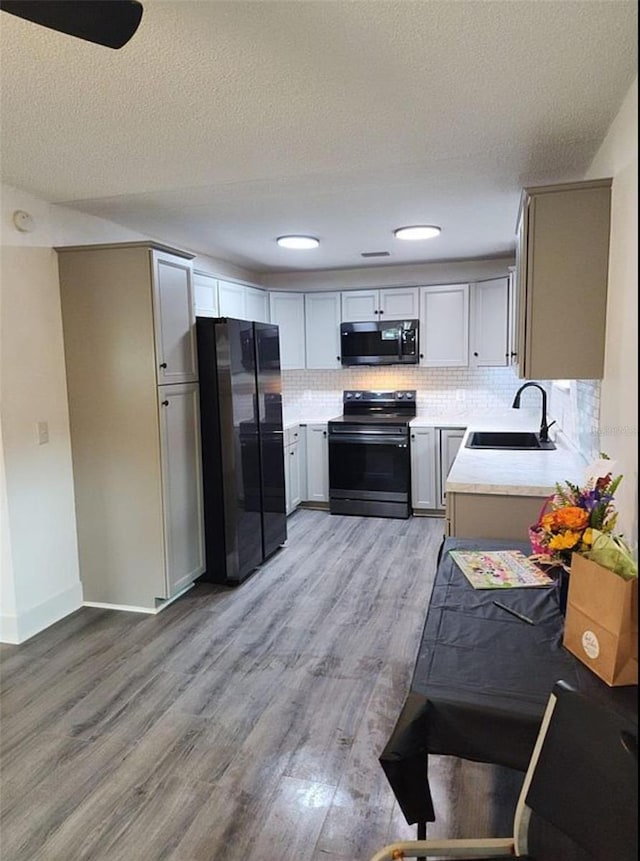 kitchen with sink, tasteful backsplash, a textured ceiling, black appliances, and light wood-type flooring