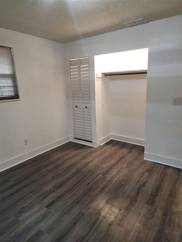 unfurnished bedroom with a textured ceiling, a closet, and dark wood-type flooring