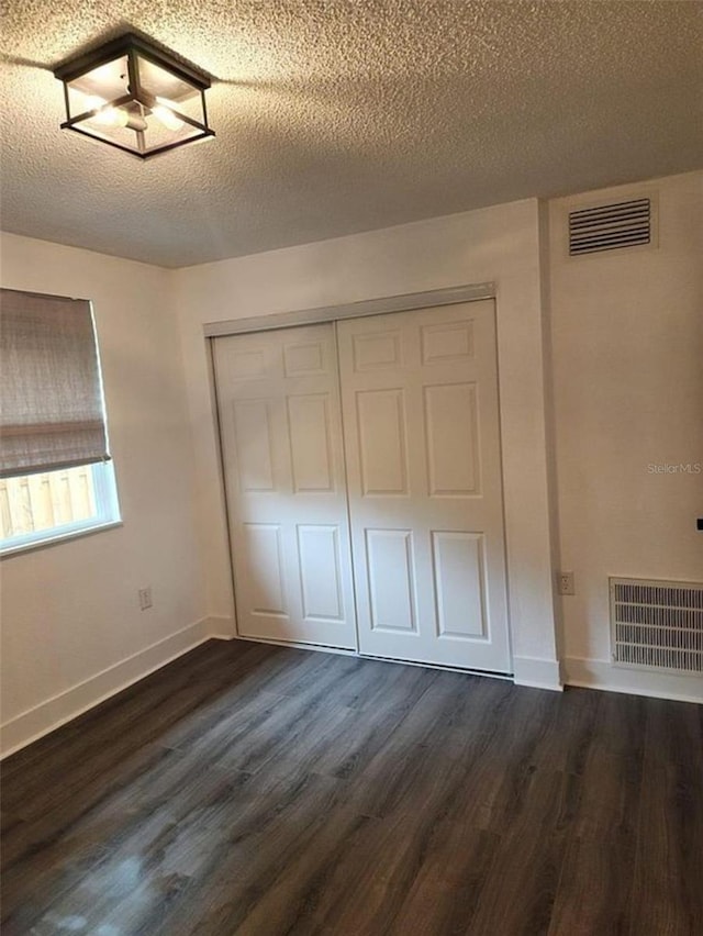 unfurnished bedroom featuring a textured ceiling, a closet, and dark wood-type flooring