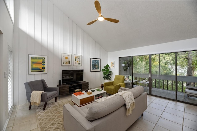 tiled living room featuring high vaulted ceiling, wood walls, ceiling fan, and a textured ceiling