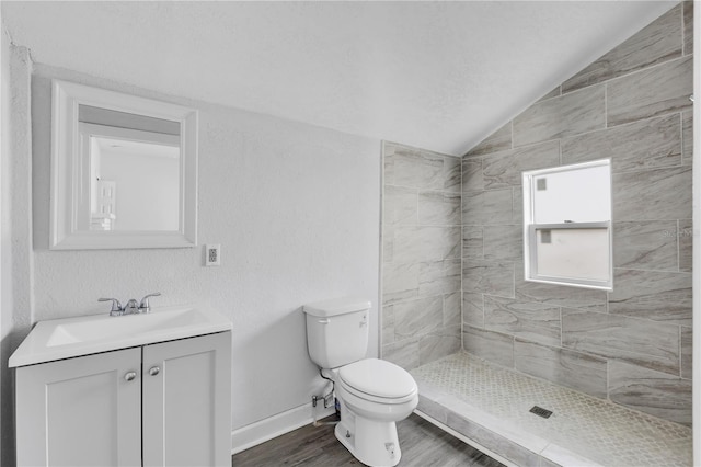 bathroom with a tile shower, hardwood / wood-style floors, toilet, lofted ceiling, and vanity