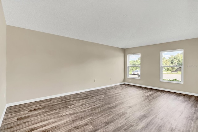 unfurnished room featuring vaulted ceiling, wood-type flooring, and a textured ceiling