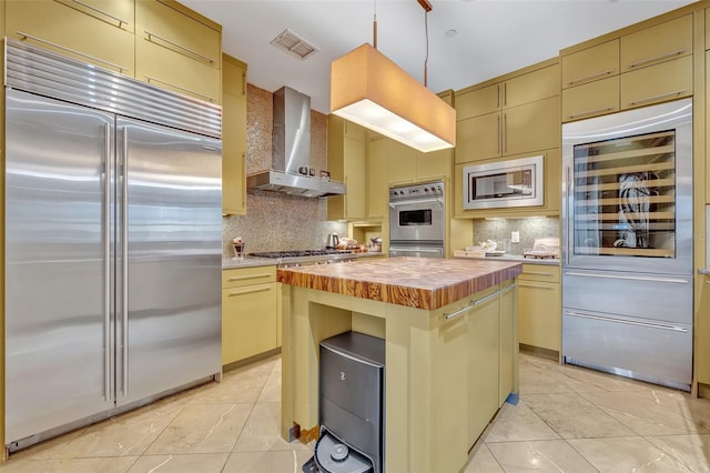 kitchen featuring wall chimney range hood, decorative backsplash, built in appliances, and a kitchen island