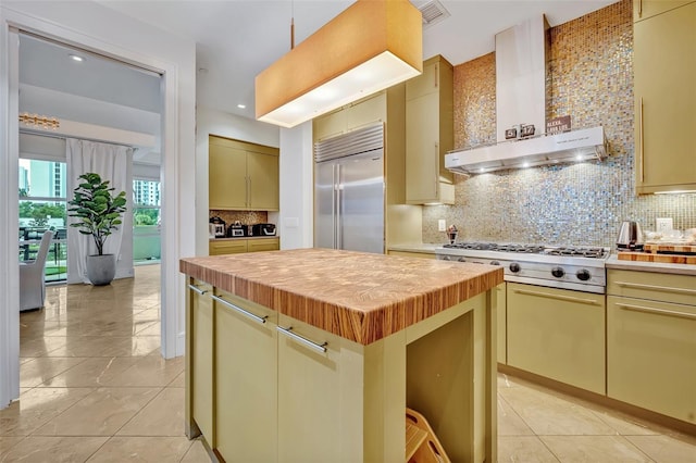 kitchen with wall chimney exhaust hood, a center island, light tile patterned floors, appliances with stainless steel finishes, and tasteful backsplash