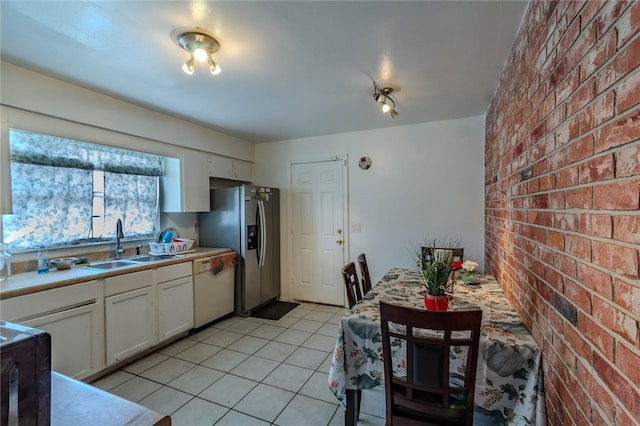 kitchen featuring stainless steel fridge, white cabinets, brick wall, white dishwasher, and sink