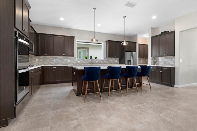 kitchen featuring appliances with stainless steel finishes, a center island, a kitchen breakfast bar, decorative light fixtures, and decorative backsplash