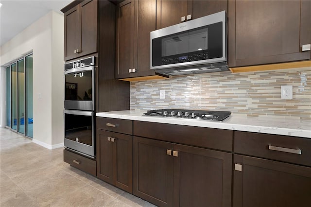 kitchen with light stone countertops, dark brown cabinets, stainless steel appliances, decorative backsplash, and light tile patterned floors