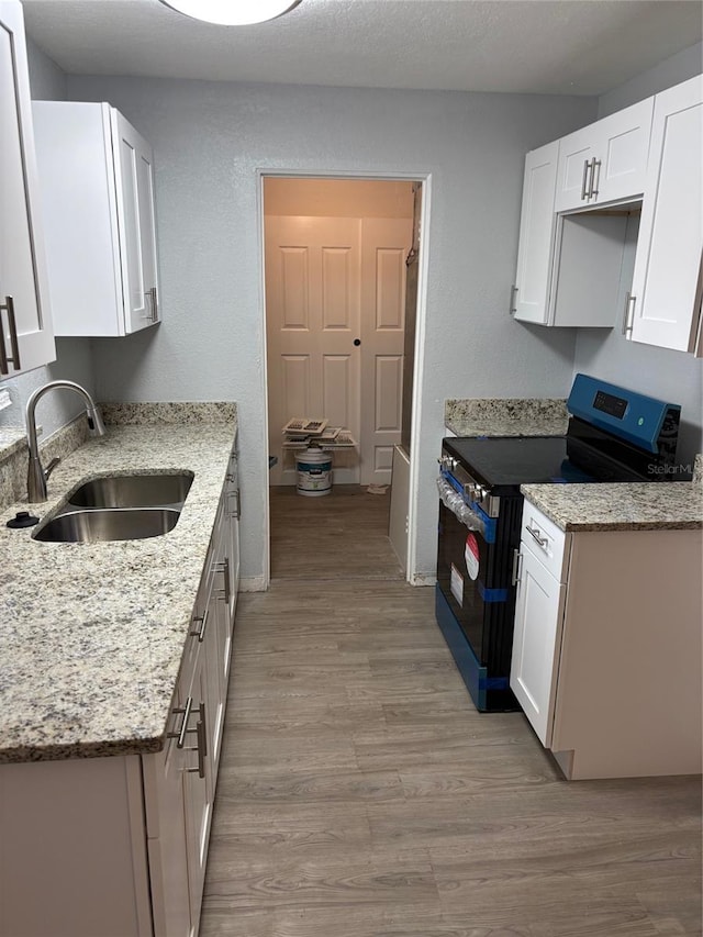 kitchen featuring light wood-type flooring, light stone counters, black range with electric cooktop, sink, and white cabinetry