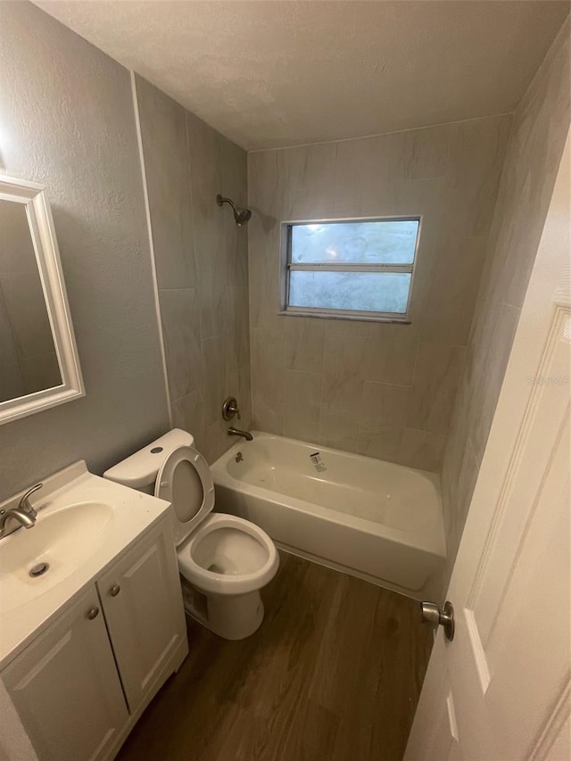 full bathroom featuring vanity, hardwood / wood-style flooring, tiled shower / bath combo, toilet, and a textured ceiling