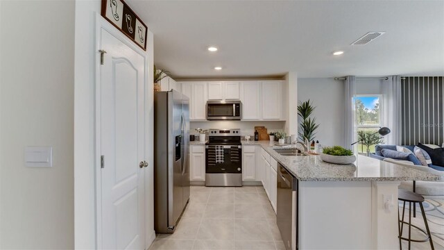 kitchen with light stone counters, white cabinets, light tile patterned floors, stainless steel appliances, and a kitchen breakfast bar