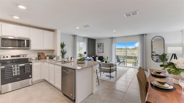 kitchen with kitchen peninsula, white cabinetry, stainless steel appliances, and light stone counters