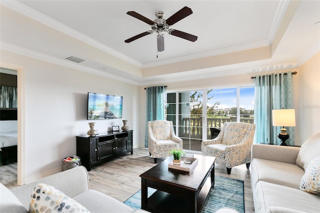 living room with ceiling fan, ornamental molding, a raised ceiling, and hardwood / wood-style floors