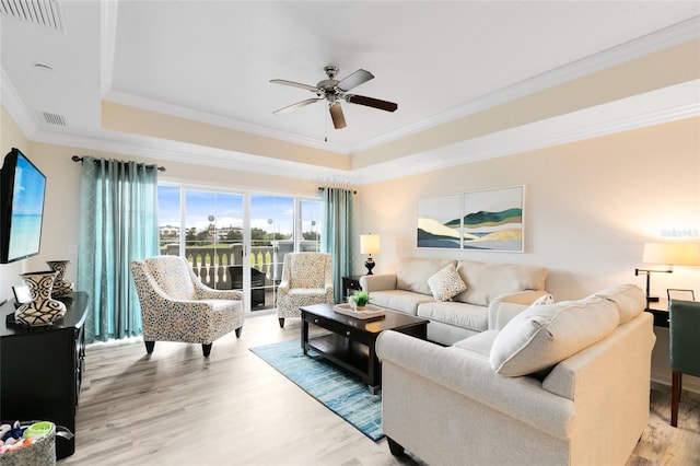 living room featuring wood-type flooring, ornamental molding, ceiling fan, and a raised ceiling