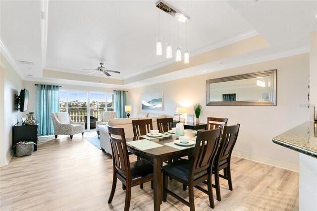 dining space featuring light wood-type flooring, crown molding, a tray ceiling, and ceiling fan