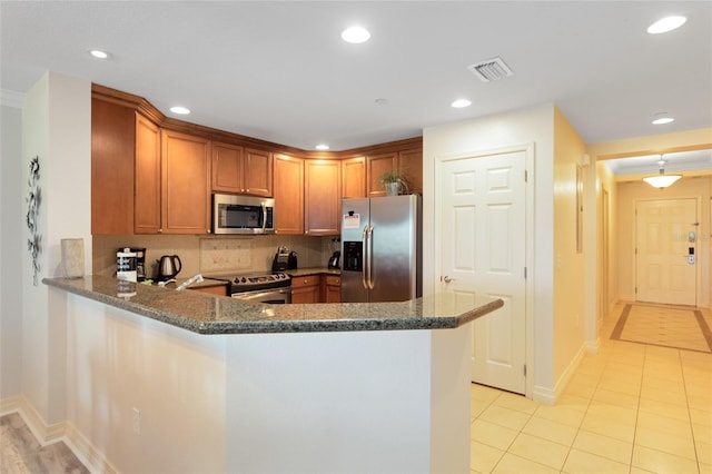 kitchen with appliances with stainless steel finishes, kitchen peninsula, dark stone counters, and tasteful backsplash