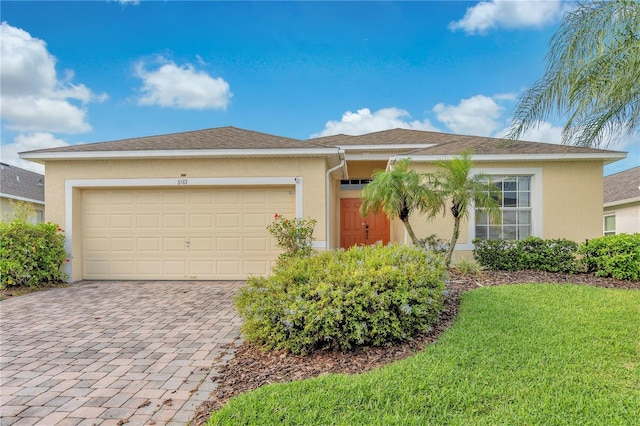 single story home featuring a front lawn, stucco siding, an attached garage, and decorative driveway