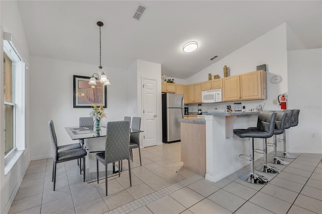 kitchen featuring kitchen peninsula, stainless steel fridge, vaulted ceiling, light brown cabinetry, and light tile patterned floors