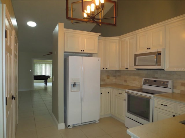 kitchen with white appliances, light tile patterned floors, an inviting chandelier, white cabinets, and pool table