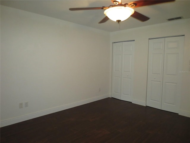 unfurnished bedroom featuring two closets, dark hardwood / wood-style floors, and ceiling fan