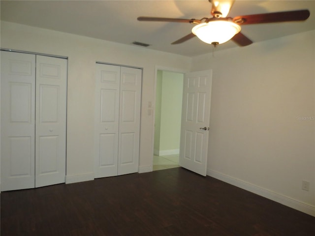 unfurnished bedroom featuring multiple closets, ceiling fan, and dark hardwood / wood-style floors