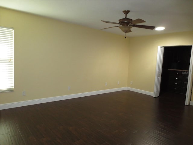 empty room with a wealth of natural light, ceiling fan, and dark wood-type flooring