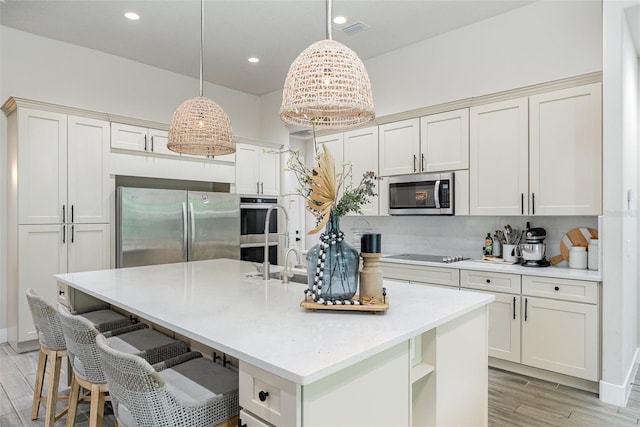 kitchen with light hardwood / wood-style floors, appliances with stainless steel finishes, backsplash, an island with sink, and pendant lighting