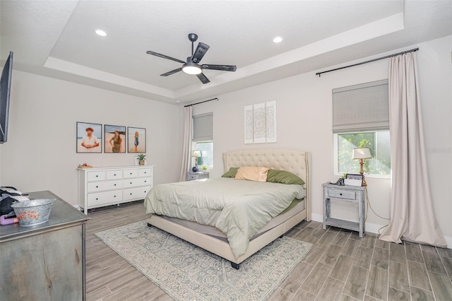 bedroom with light hardwood / wood-style floors, ceiling fan, and a raised ceiling