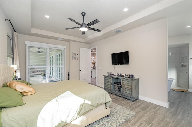 bedroom with light wood-type flooring, a textured ceiling, a raised ceiling, ceiling fan, and ensuite bathroom