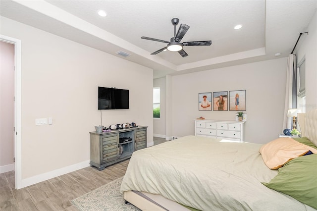 bedroom with a textured ceiling, light wood-type flooring, ceiling fan, and a tray ceiling