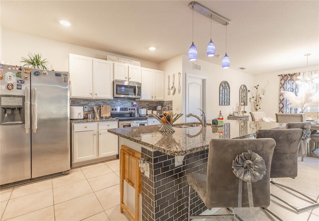 kitchen featuring dark stone countertops, appliances with stainless steel finishes, white cabinetry, and pendant lighting