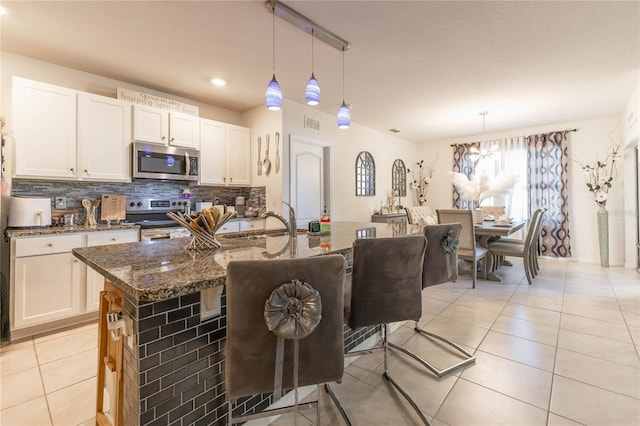 kitchen featuring appliances with stainless steel finishes, white cabinets, dark stone counters, and pendant lighting