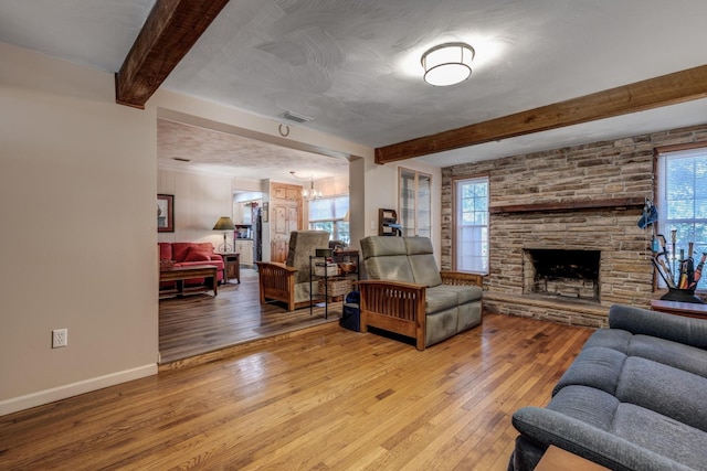 living room with beamed ceiling, a stone fireplace, wood-type flooring, and an inviting chandelier