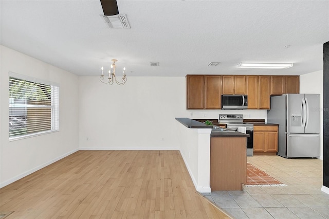 kitchen featuring a textured ceiling, kitchen peninsula, stainless steel appliances, light hardwood / wood-style flooring, and an inviting chandelier