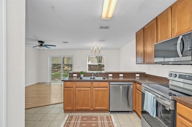 kitchen with appliances with stainless steel finishes, light tile patterned flooring, sink, ceiling fan with notable chandelier, and kitchen peninsula