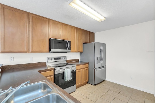 kitchen with appliances with stainless steel finishes, a textured ceiling, sink, and light tile patterned floors